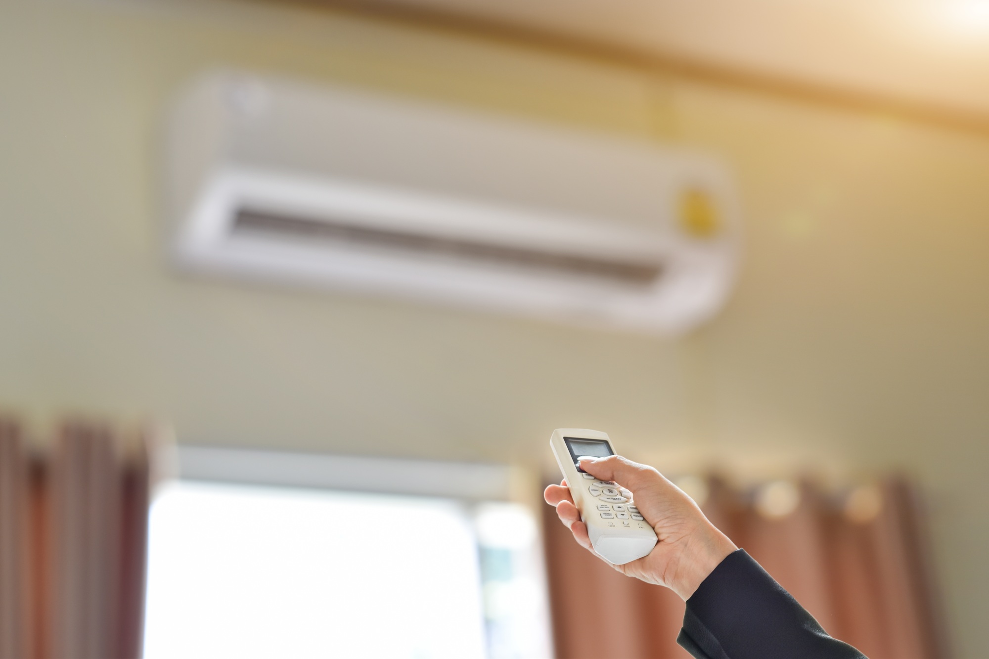 Close up of businessman hand holding remote control directed adjusting of air conditioner.