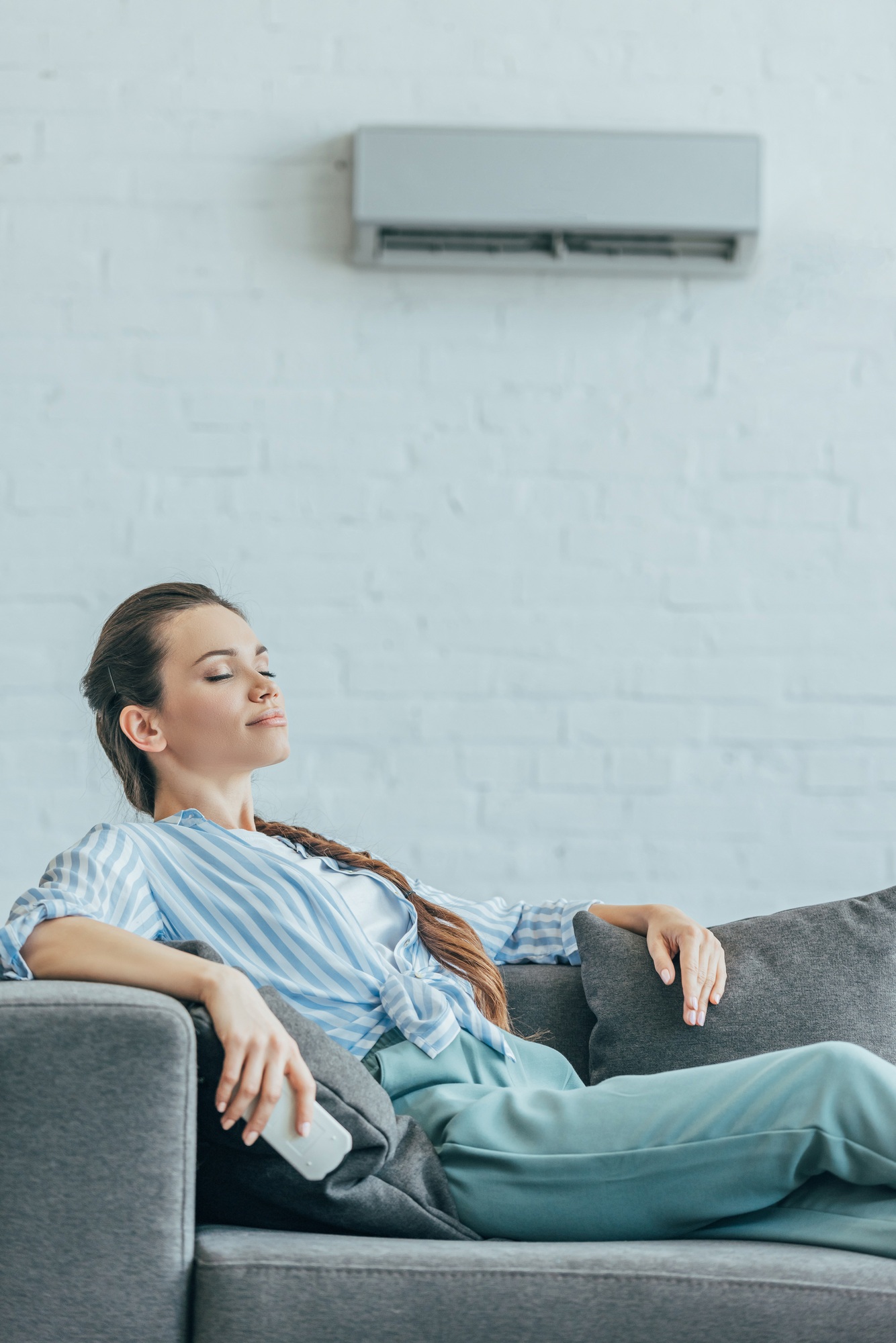 woman resting on sofa with air conditioner on wall, summer heat concept